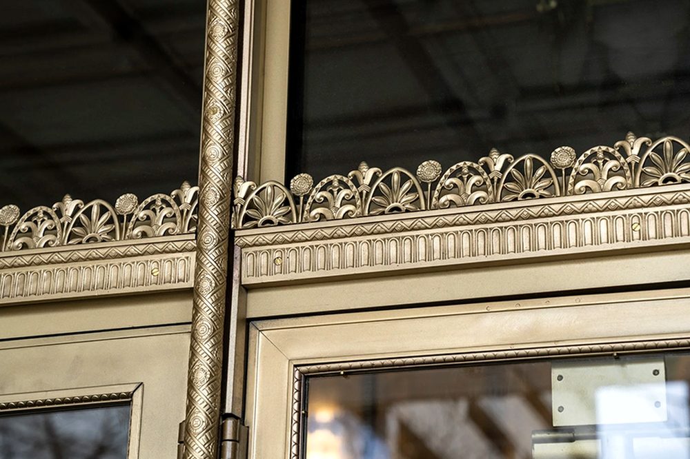 Bronze thistle frieze and saddle-and-rope detail on a storefront entrance after restoration to its original luster