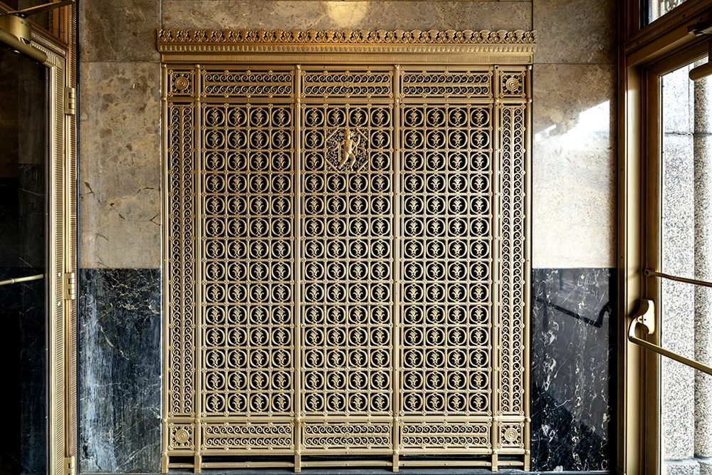 Vestibule bronze ornamental HVAC grille after repair and refinishing, with refurbished marble cladding